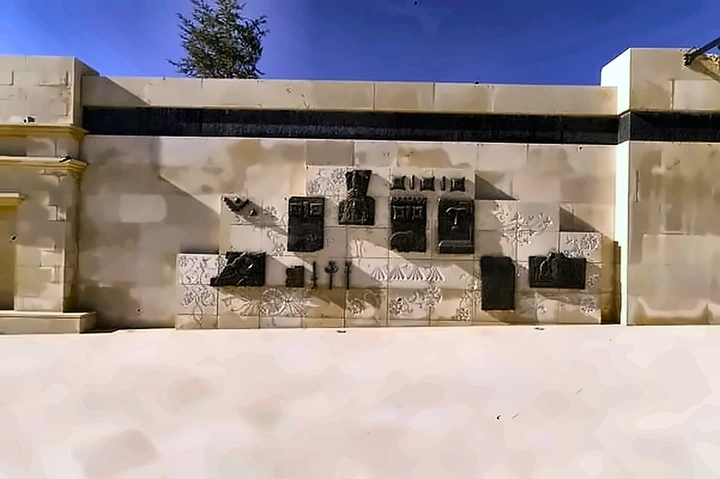 A stone courtyard wall carrying a spaced line of dark bronze relief panels of varying sizes.