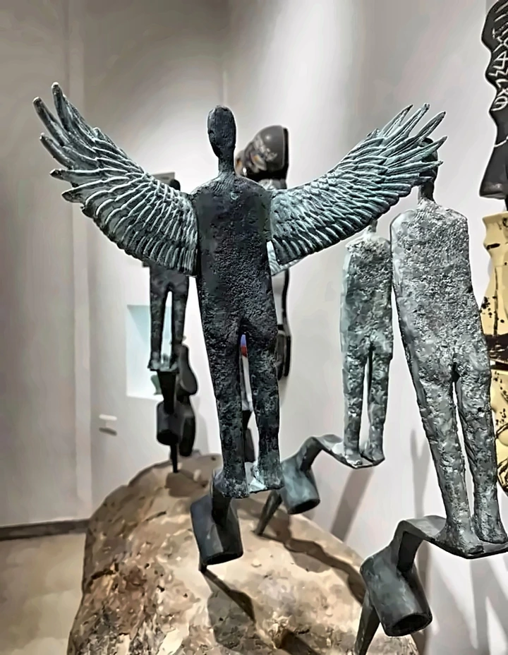 A winged bronze figure on a boulder among figures without wings.