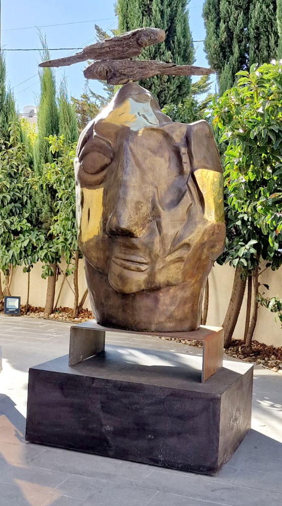 A large sculpted head topped by fish forms, outdoors.