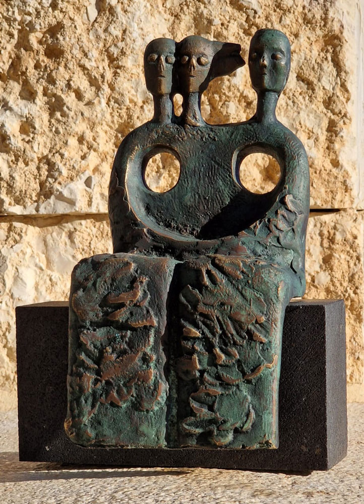 A seated form with three heads and two circular openings.