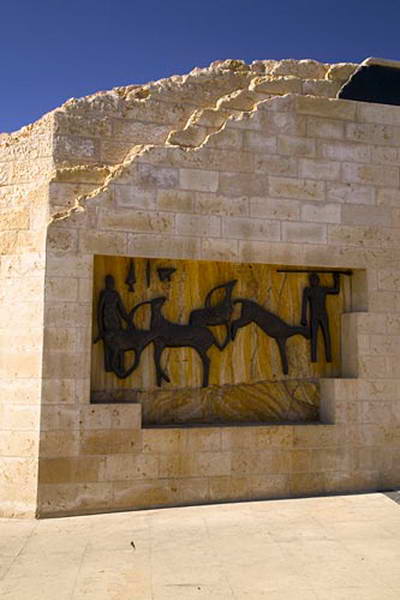 The same relief seen from further back, showing it built into the facade of a stone building under a deep blue sky.