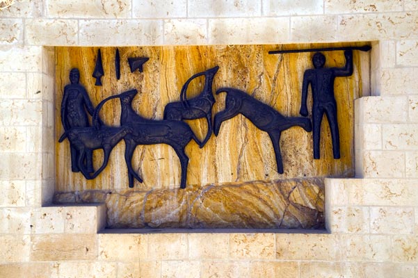 A bronze hunting relief set into a recess in a stone wall, against a ground of veined golden onyx: two figures with spears and three animals.