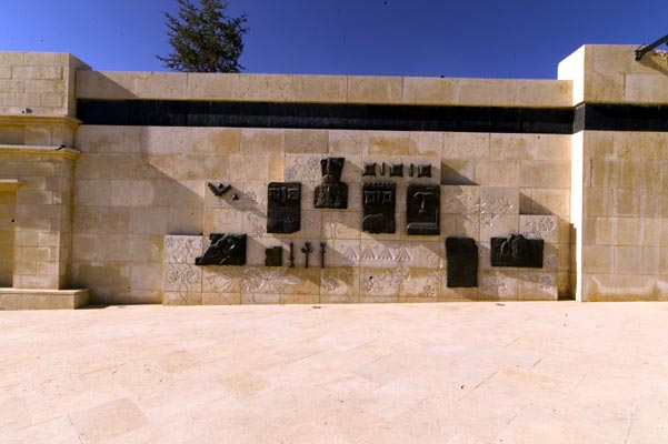 A stone courtyard wall carrying a spaced line of dark bronze relief panels of varying sizes.