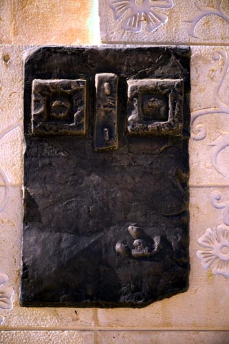 A single dark panel: two square eye forms above a mouth, on a carved stone ground.
