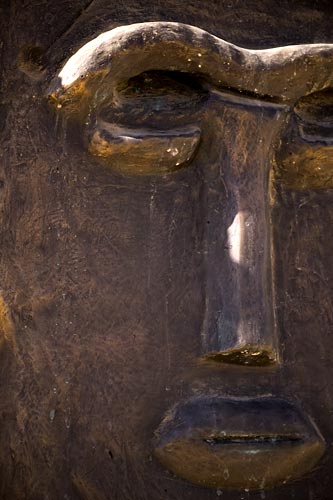 Close detail of a bronze face — the brow, the long nose and the lips catching light.