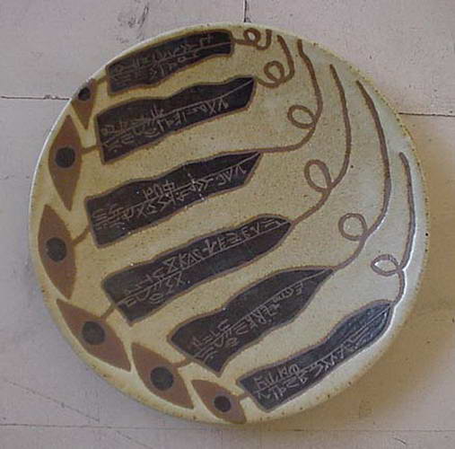 A pale plate with six dark tapering bands of incised script curving across it, a border of eyes below.