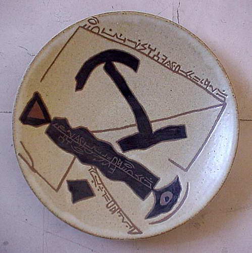 A cream plate with a large black anchor form and lines of script running along the rim and through the centre.